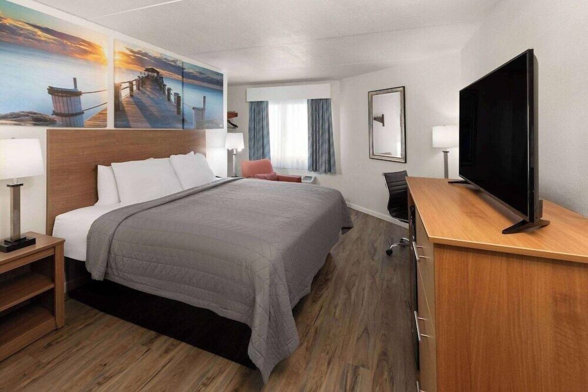 A hotel room with a bed, a desk, a television, and artwork on the walls.