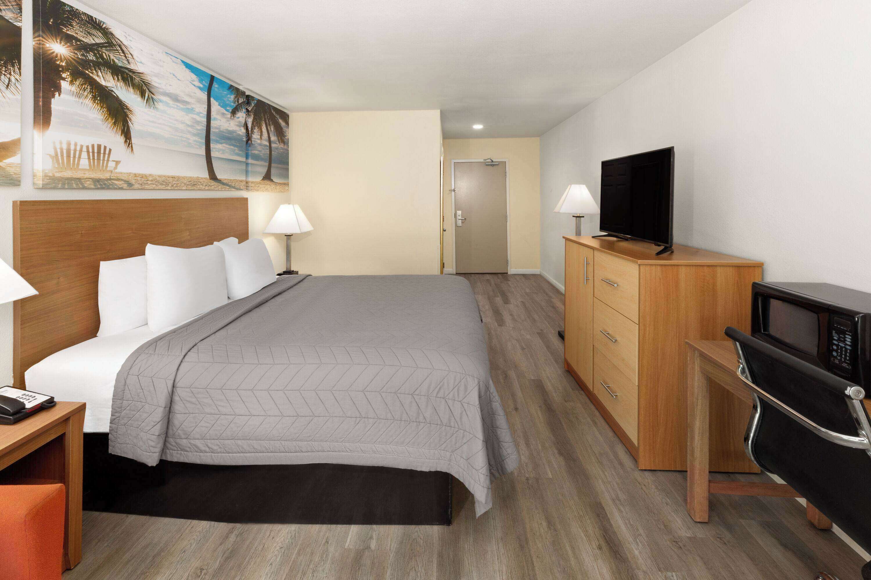 Una habitación de hotel con cama, lámparas de noche, televisor, escritorio y silla.