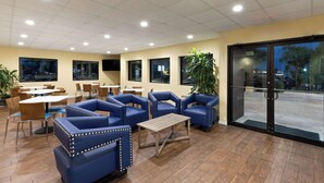 A restaurant with blue upholstered booths, wooden tables, and potted plants. - Days Inn by Wyndham Biloxi Beach (Biloxi)