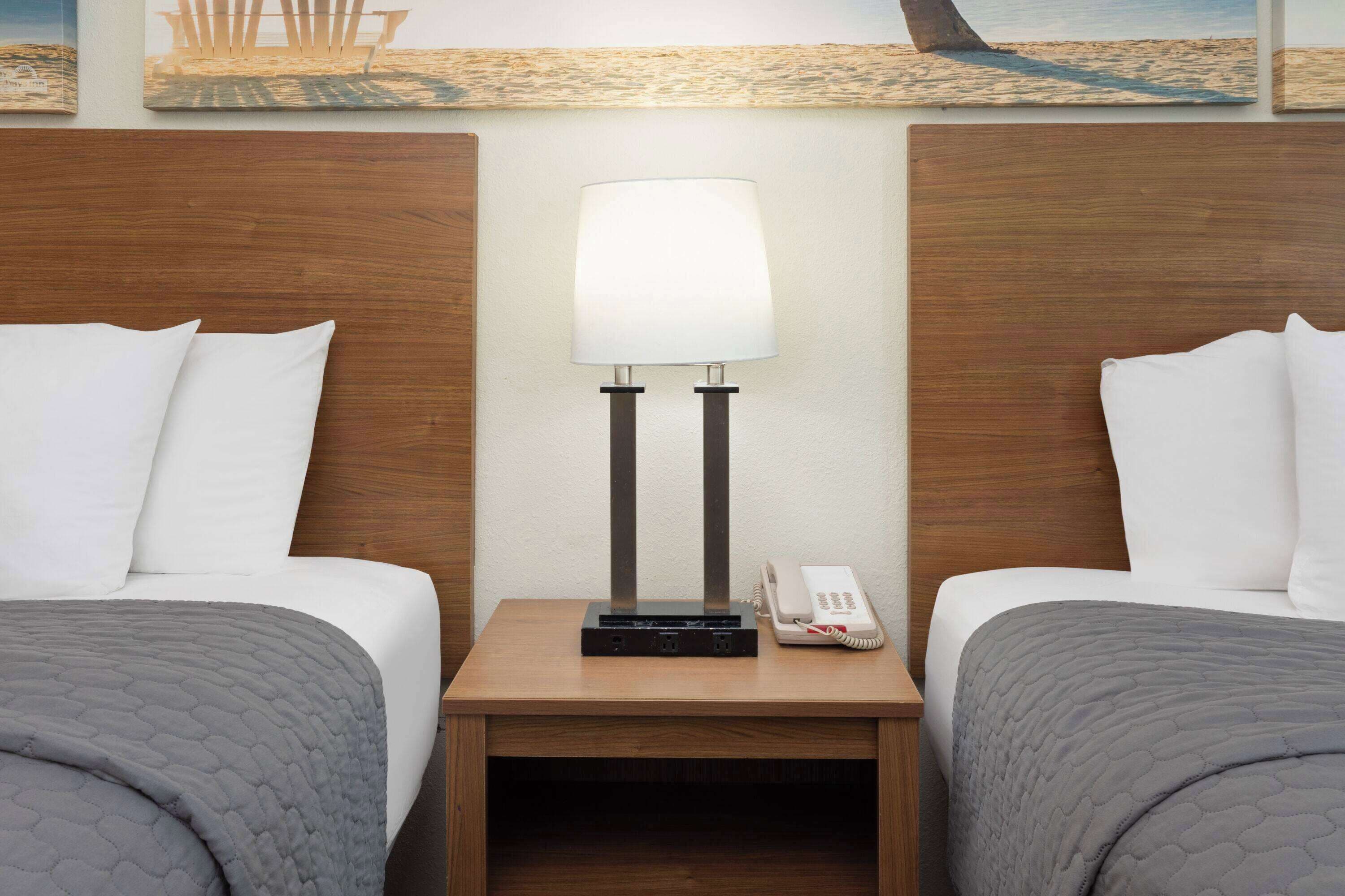 A hotel room with two beds, a nightstand with a lamp, a phone, and artwork on the wall.