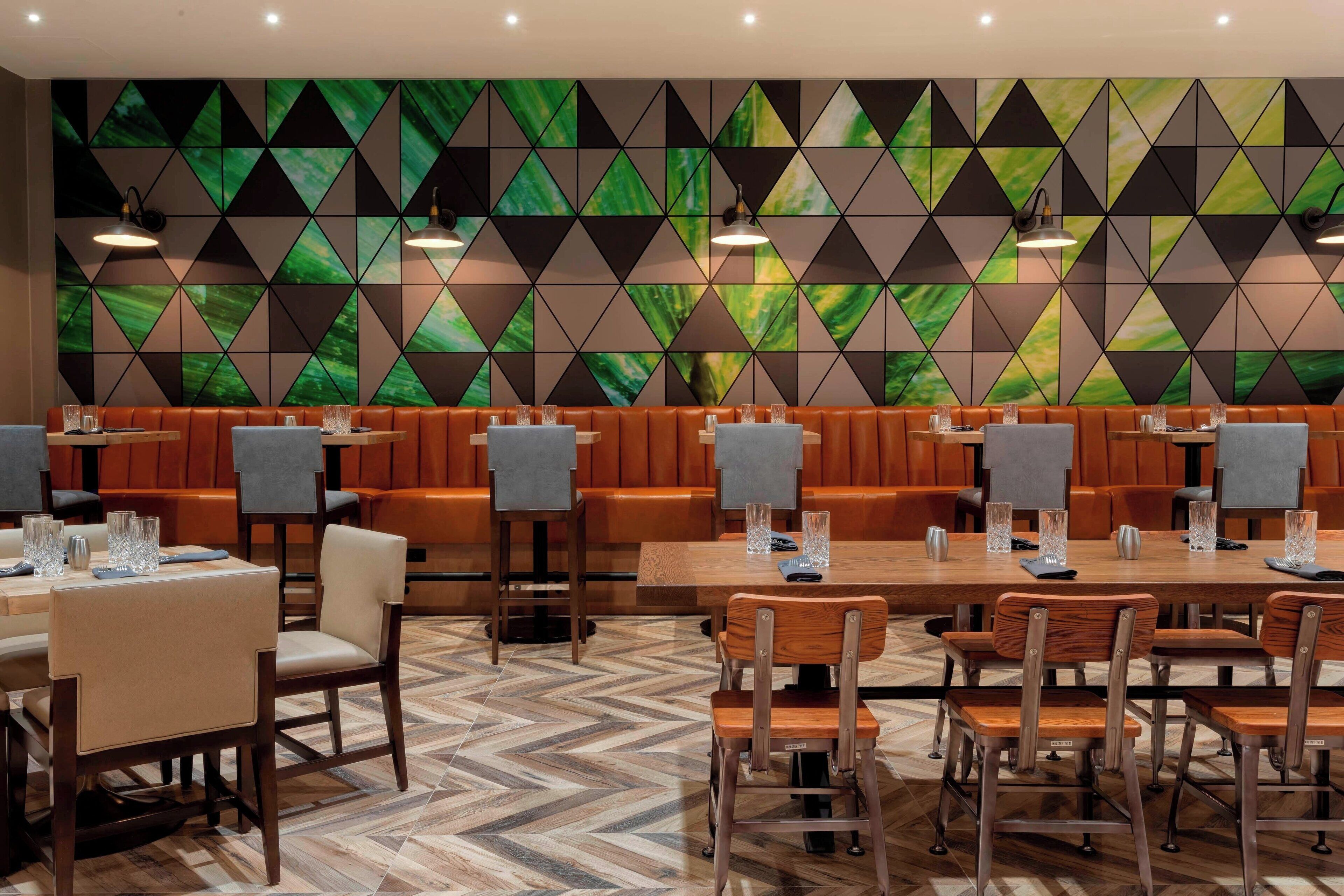 Un restaurant dont le sol est décoré d’un motif en chevrons, avec des tables et des chaises en bois, et un mur orné d’un motif géométrique.