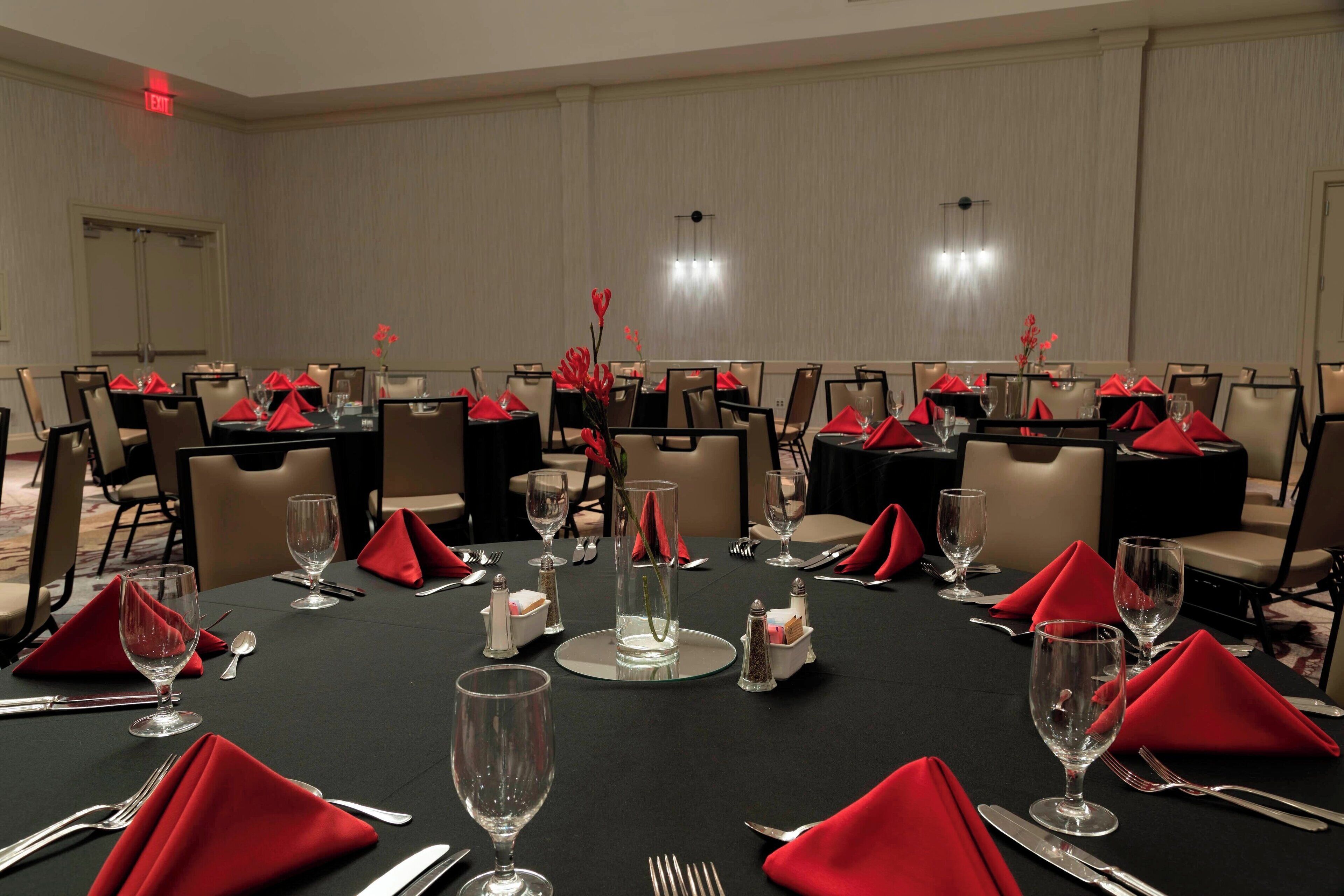 A conference room with multiple tables set for dining, each with red napkins, silverware, and clear glassware.
