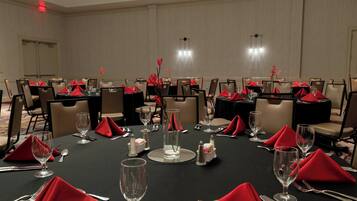A conference room with multiple tables set for dining, each with red napkins, silverware, and clear glassware.