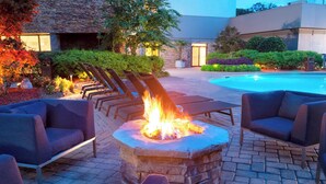 A stone fire pit surrounded by lounge chairs, a pool, and a building with a stone facade. - Atlanta Marriott Northeast/Emory Area (Atlanta)