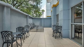 An outdoor patio area with multiple tables and chairs, a tiled floor, and a building with large windows.