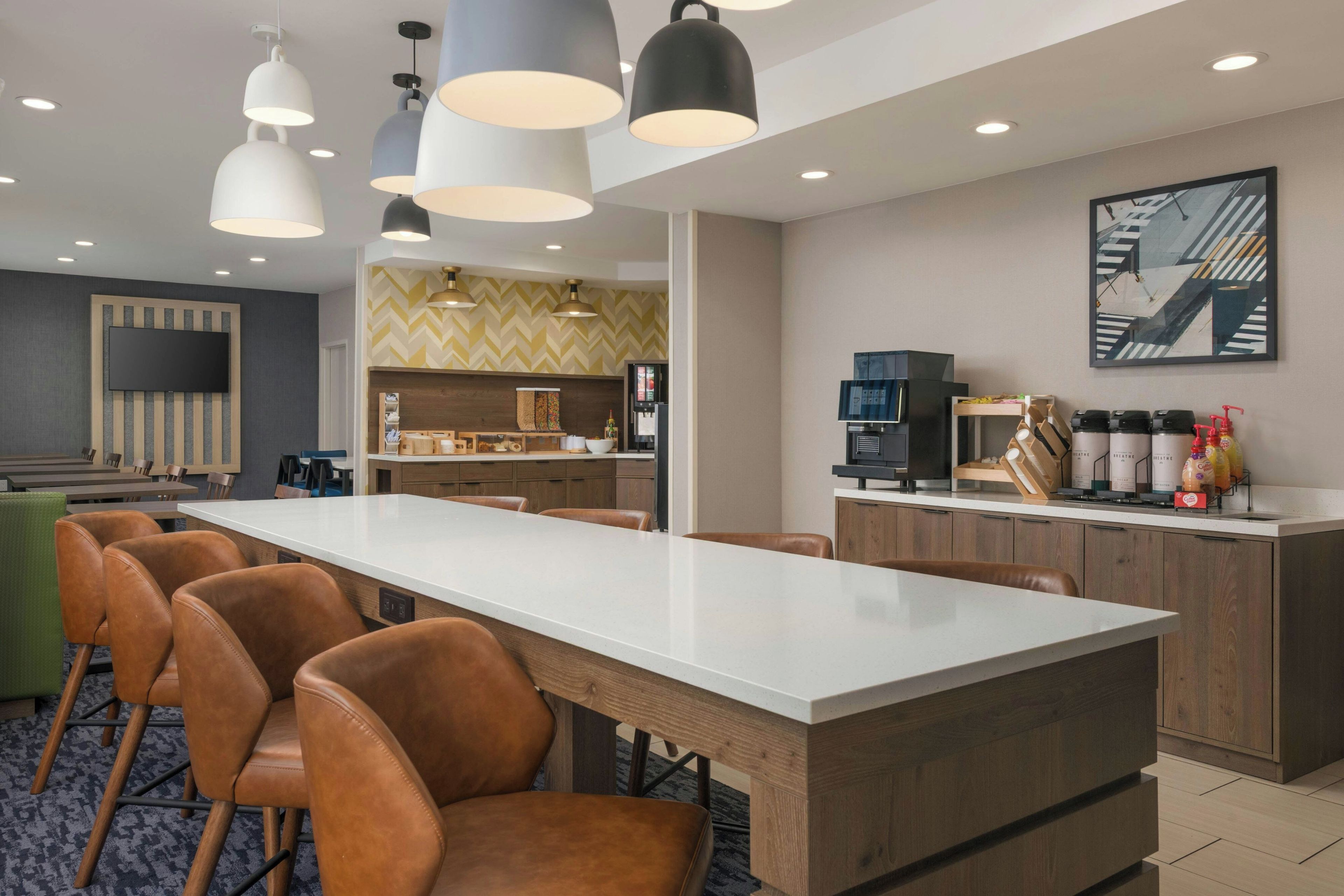 Una habitación de hotel moderna con una larga mesa de comedor, sillas de cuero, una zona de cocina y un amplio ventanal.