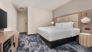 A modern hotel room with a large bed, a TV, a desk, and a carpeted floor.