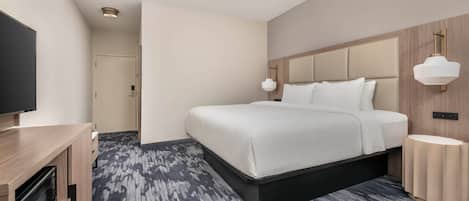 Una habitación de hotel moderna con una cama grande, televisión, escritorio y piso alfombrado.