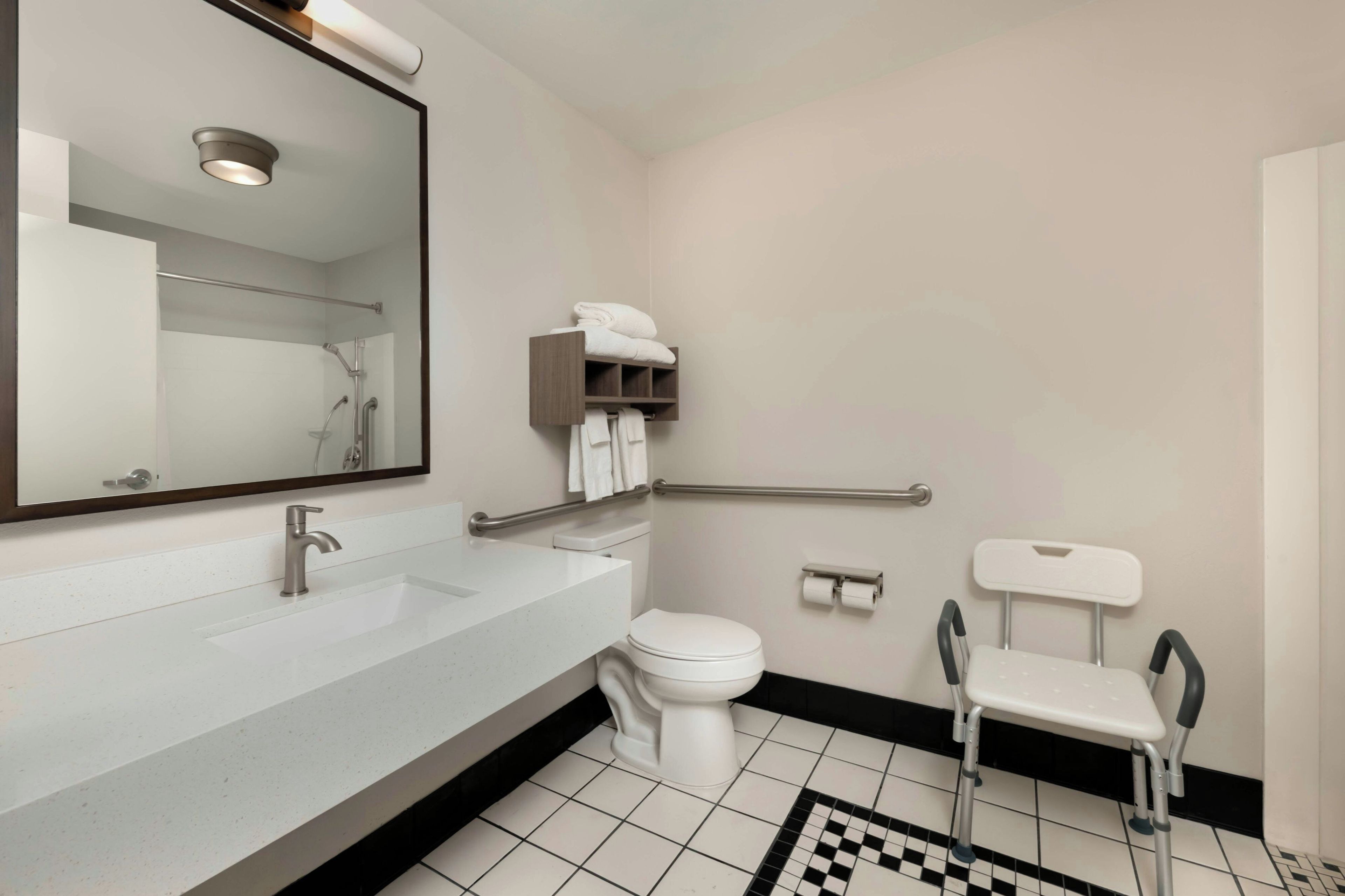 Une salle de bain moderne avec un lavabo blanc, des toilettes, un miroir et une barre d’appui.