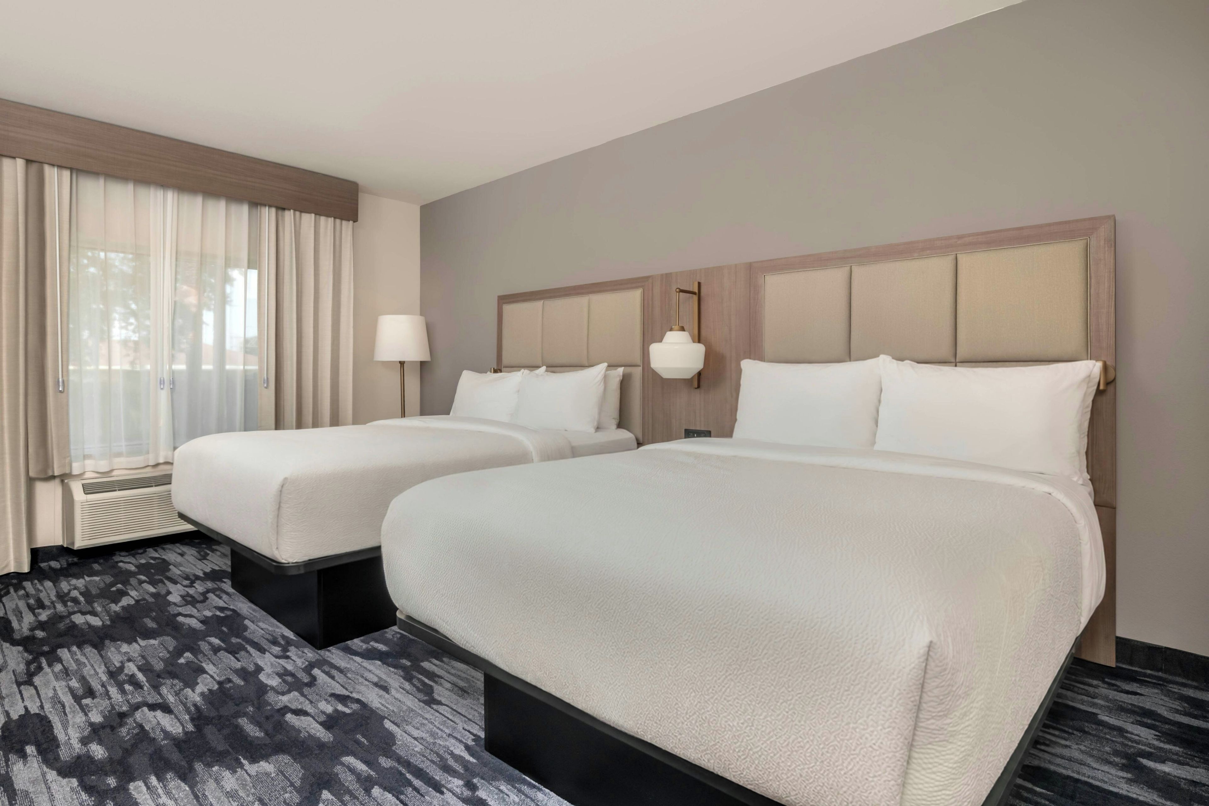 Een hotelkamer met twee bedden, een groot raam met gordijnen, een wandlamp en een vloerbedekking.