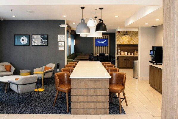 A modern hotel lobby with a long communal table, seating, a reception desk, and a Viasat sign. - City Express By Marriott Lafayette (Lafayette)