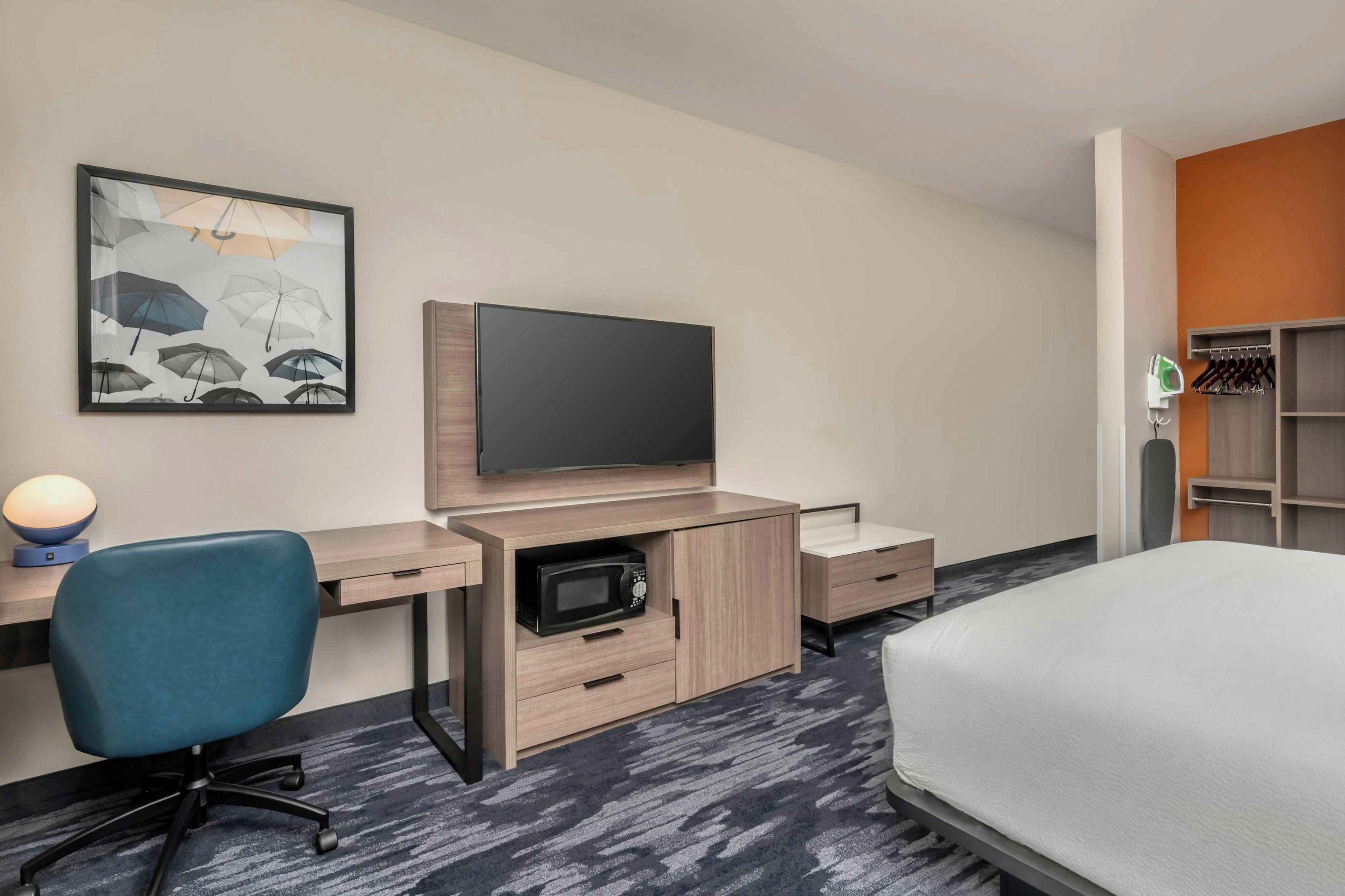 A hotel room with a bed, a desk with a flat-screen TV, a chair, a microwave, and a wardrobe.
