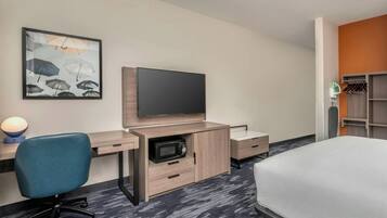 A hotel room with a bed, a desk with a flat-screen TV, a chair, a microwave, and a wardrobe.