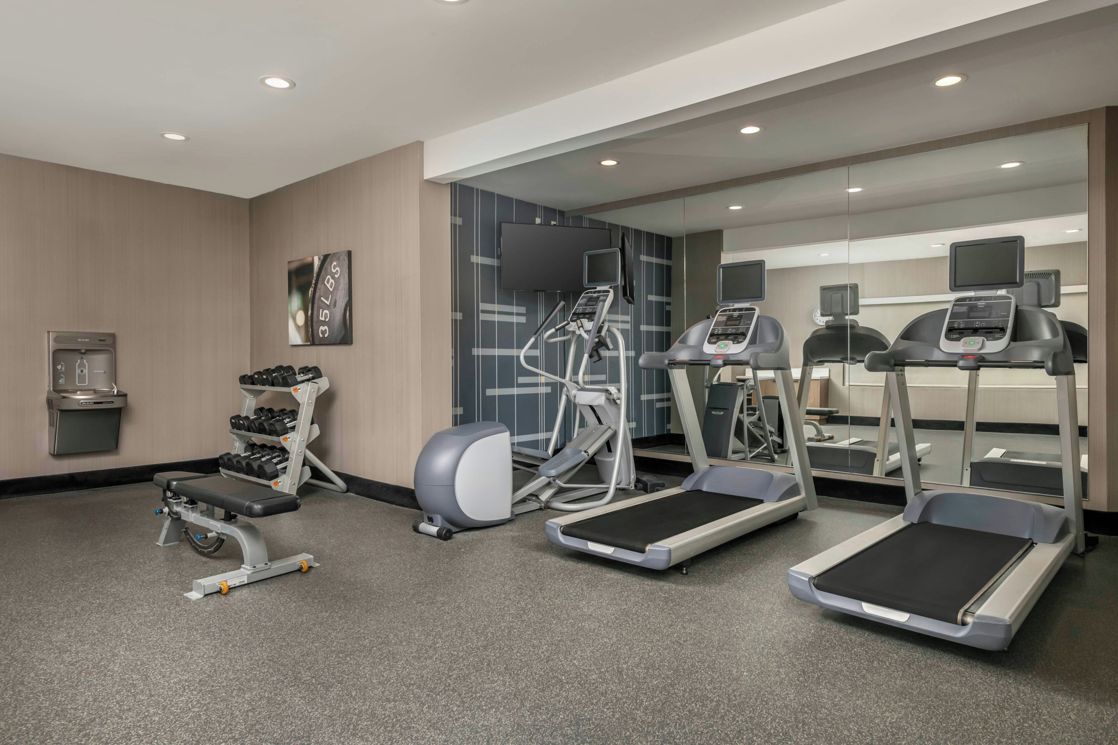 A gym with treadmills, an elliptical, a bench, and a dumbbell rack.