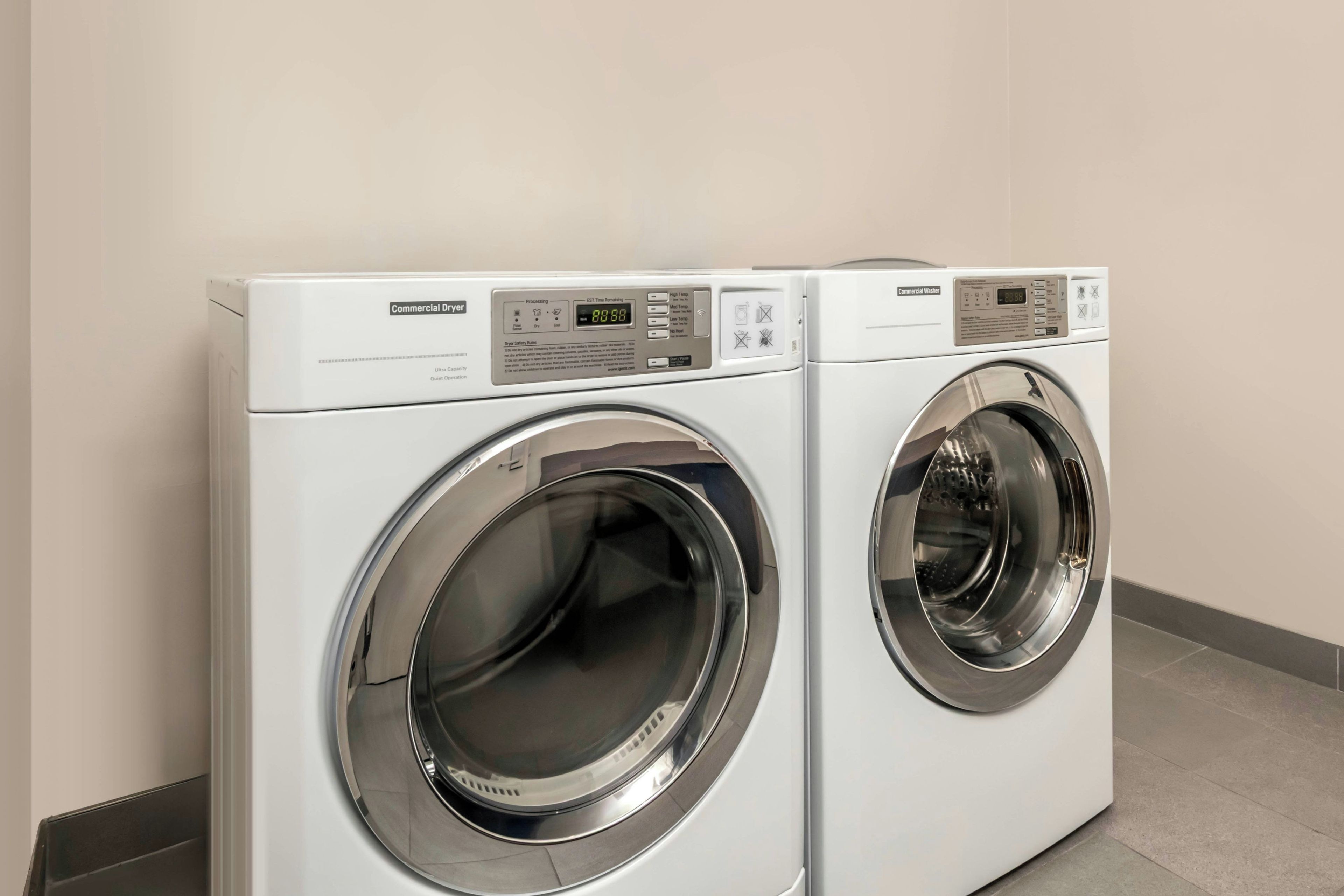 Deux sèche-linge commerciaux sont placés côte à côte dans une pièce dont les murs sont de couleur neutre et dont le sol est carrelé.