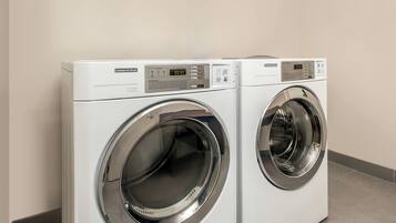 Deux sèche-linge commerciaux sont placés côte à côte dans une pièce dont les murs sont de couleur neutre et dont le sol est carrelé.