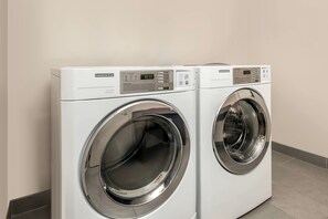 Two commercial dryers side by side in a room with a plain wall and tiled floor. - City Express By Marriott Lafayette (Lafayette)