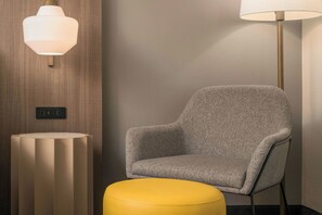 A modern room with a grey upholstered armchair, a yellow ottoman, and two wall-mounted lamps. - City Express By Marriott Lafayette (Lafayette)