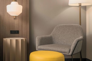 Ein modernes Zimmer mit einem grau gepolsterten Sessel, einem gelben Hocker und zwei Wandleuchten.
