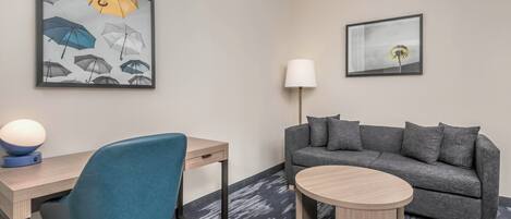 Et hotelværelse med skrivebord, stol, sofa, lampe og billedkunst på væggene.