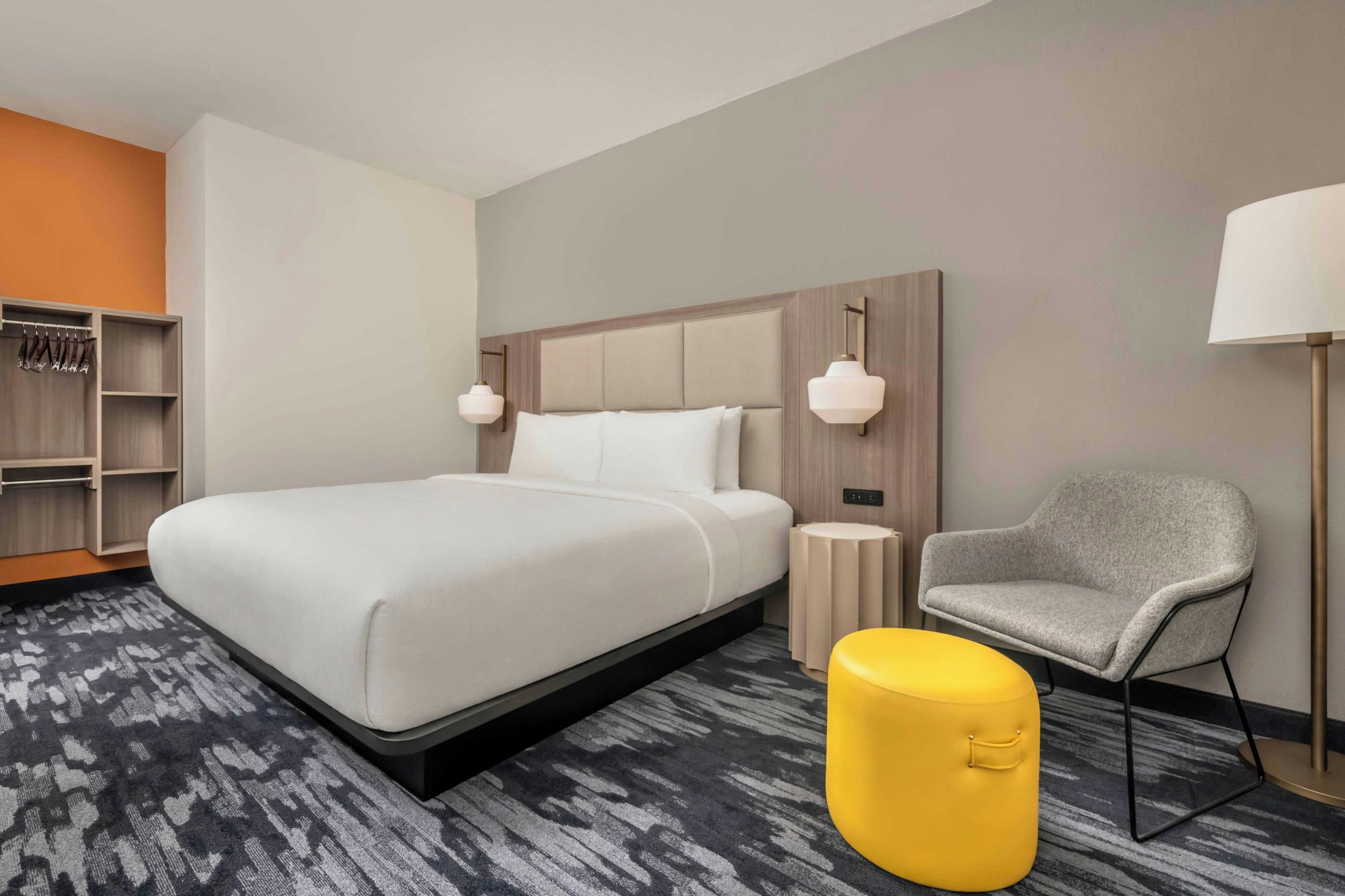 Een hotelkamer met een groot bed, nachtkastje, stoel, lamp en garderobe.