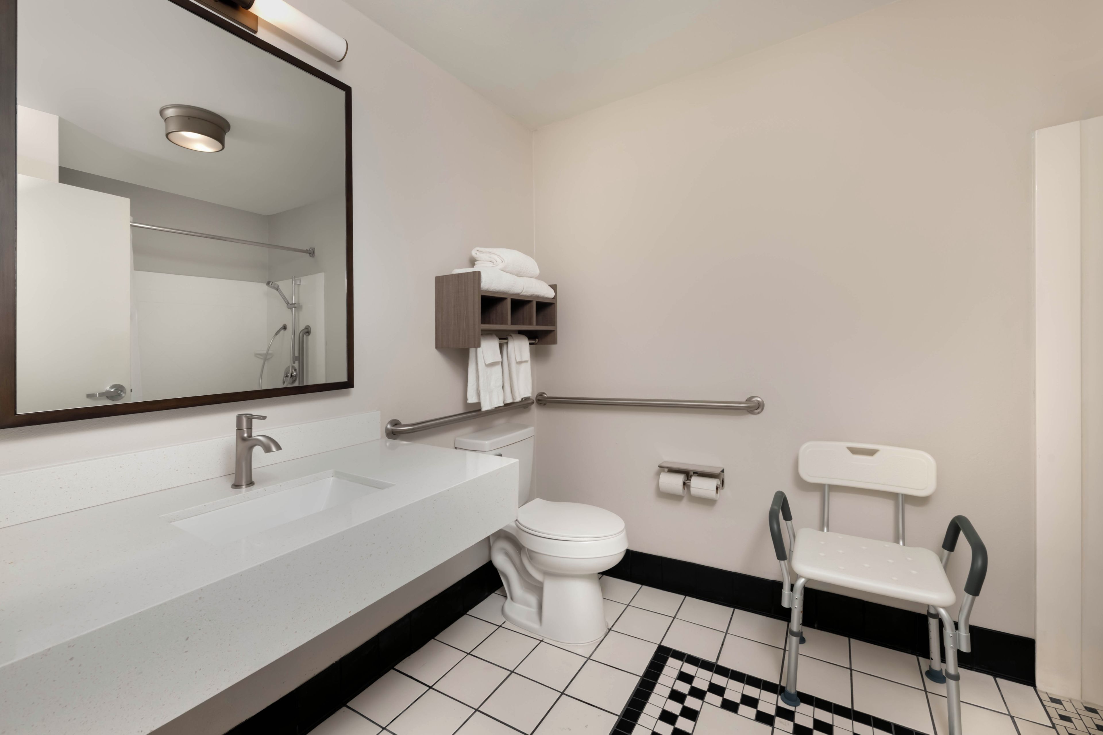 Une salle de bain moderne avec un lavabo blanc, des toilettes, un miroir et une barre d’appui.