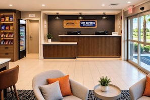 A hotel lobby with a reception desk, vending machines, seating area, and a large window.