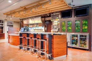A bar area with wooden bar stools, a refrigerated display case with bottles, and a menu board. - Courtyard by Marriott Raleigh Crabtree Valley (Raleigh)