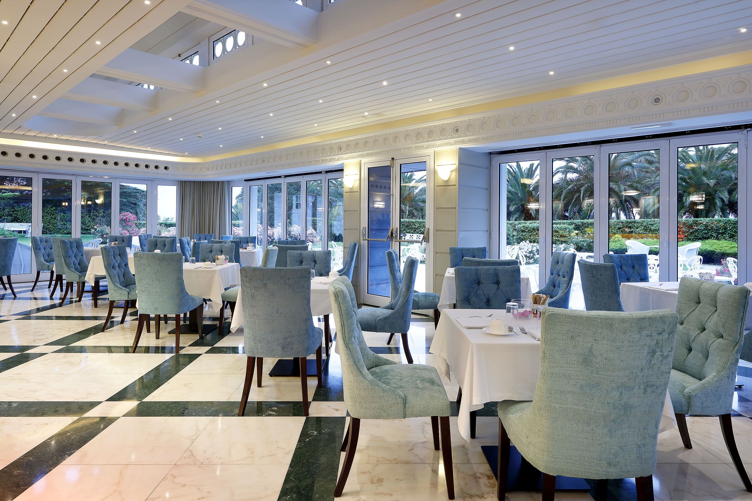 A dining area with light blue upholstered chairs, white tables, and a checkered floor pattern.