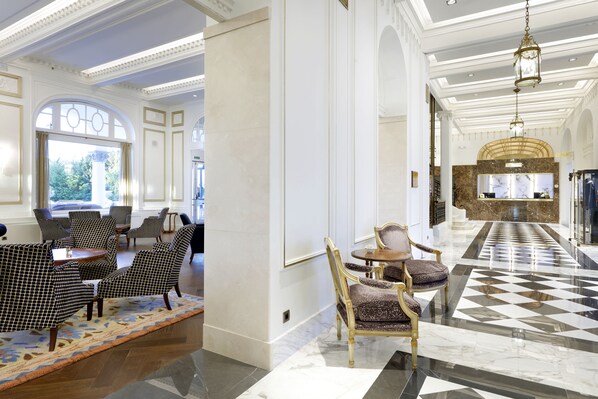 A lobby with a checkered floor, patterned chairs, and a marble reception desk.