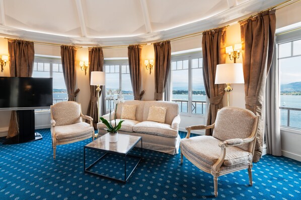 A room with a sofa, two armchairs, a coffee table, a TV, and a view of the sea.