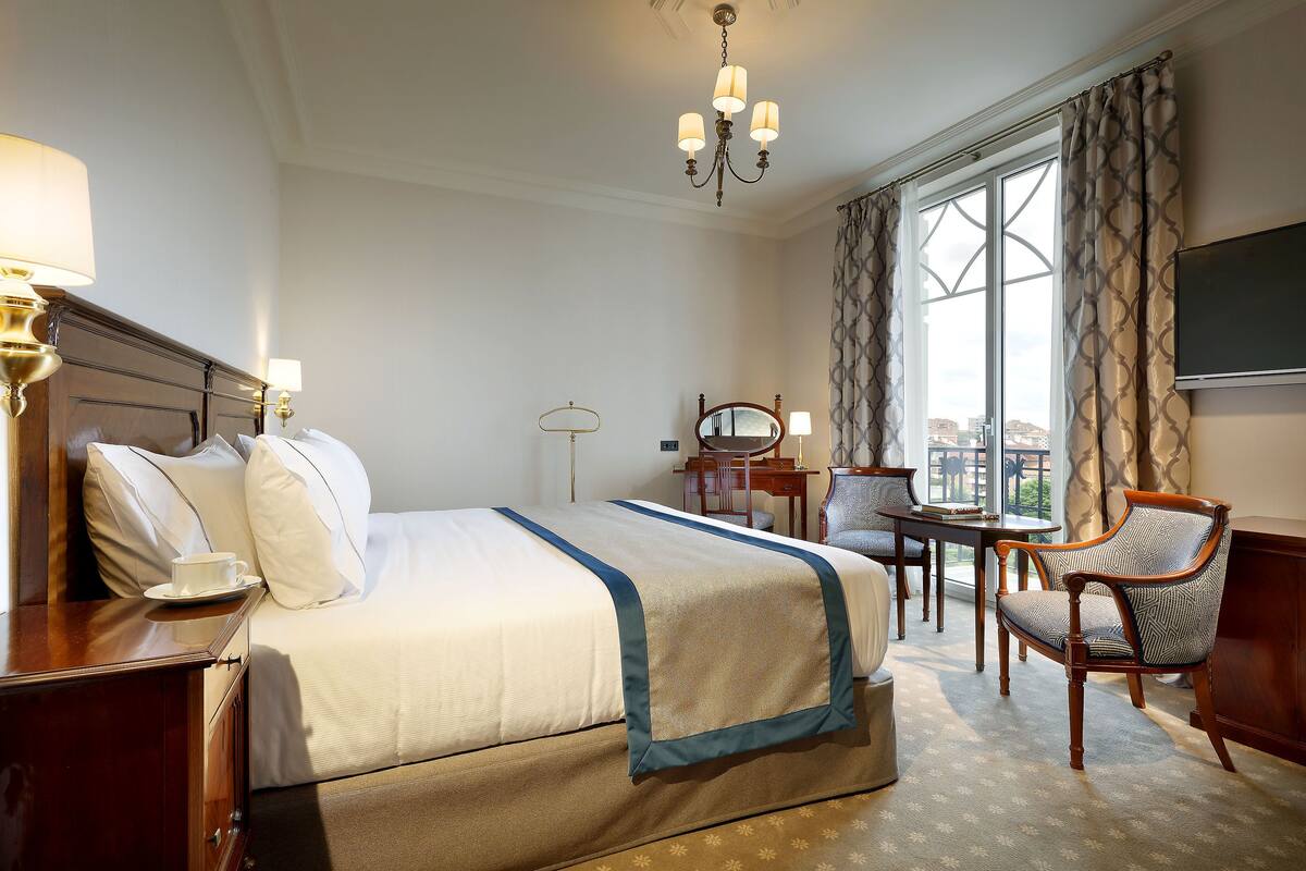 A hotel room with a large bed, a desk, a chair, and a television.