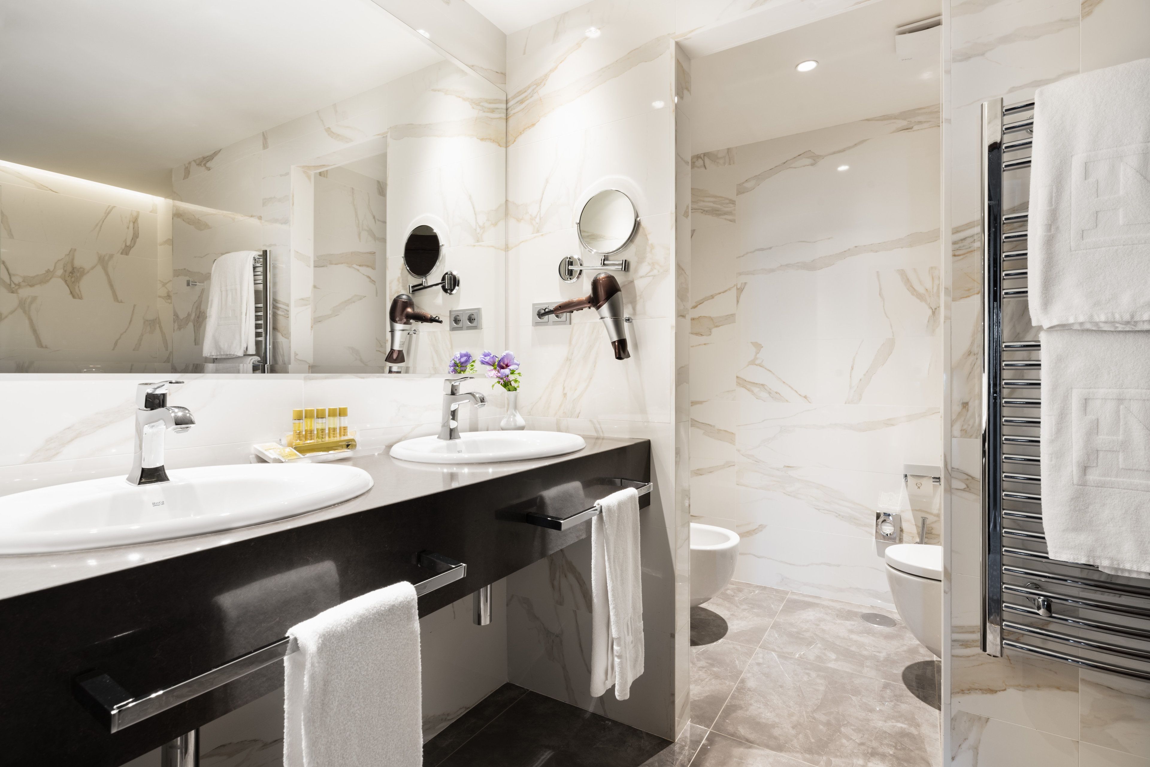Un baño moderno con dos lavamanos, un secador de pelo, un espejo y un perchero para toallas.