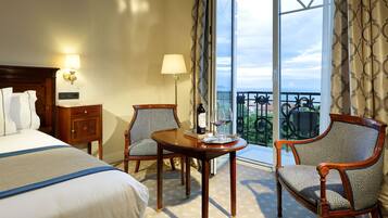 A hotel room with a bed, two chairs, a small table, and a balcony with a view.