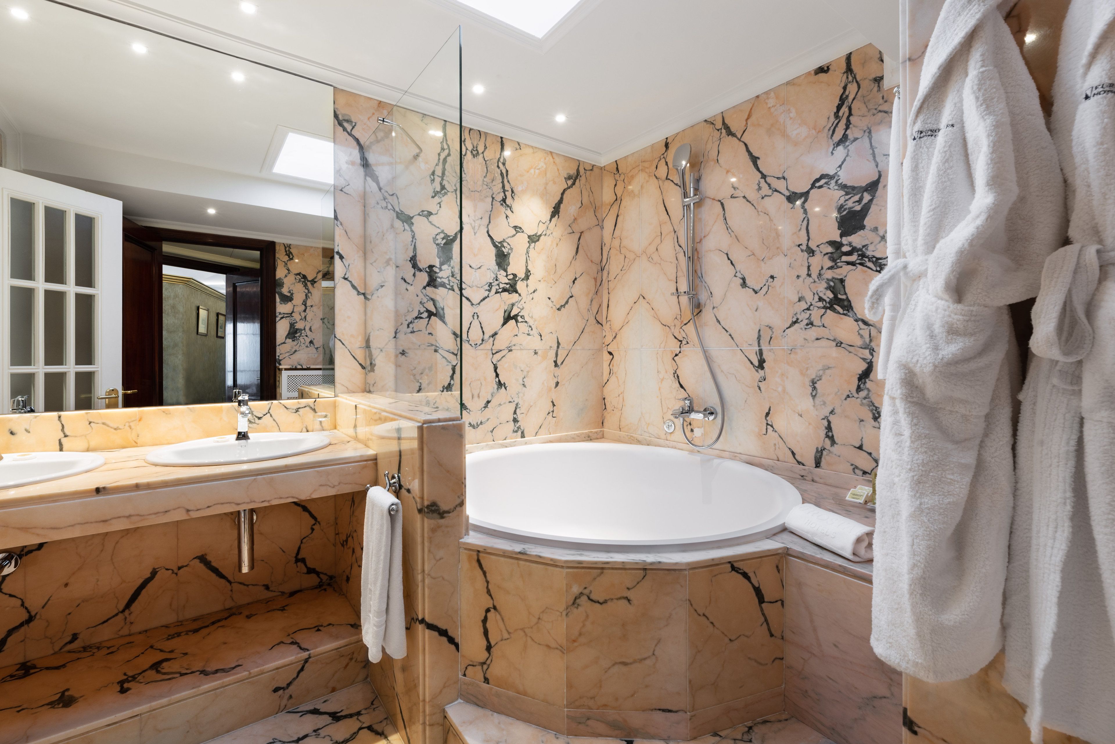 Une salle de bain moderne avec des murs en marbre, une grande baignoire et un meuble-lavabo à deux vasques.