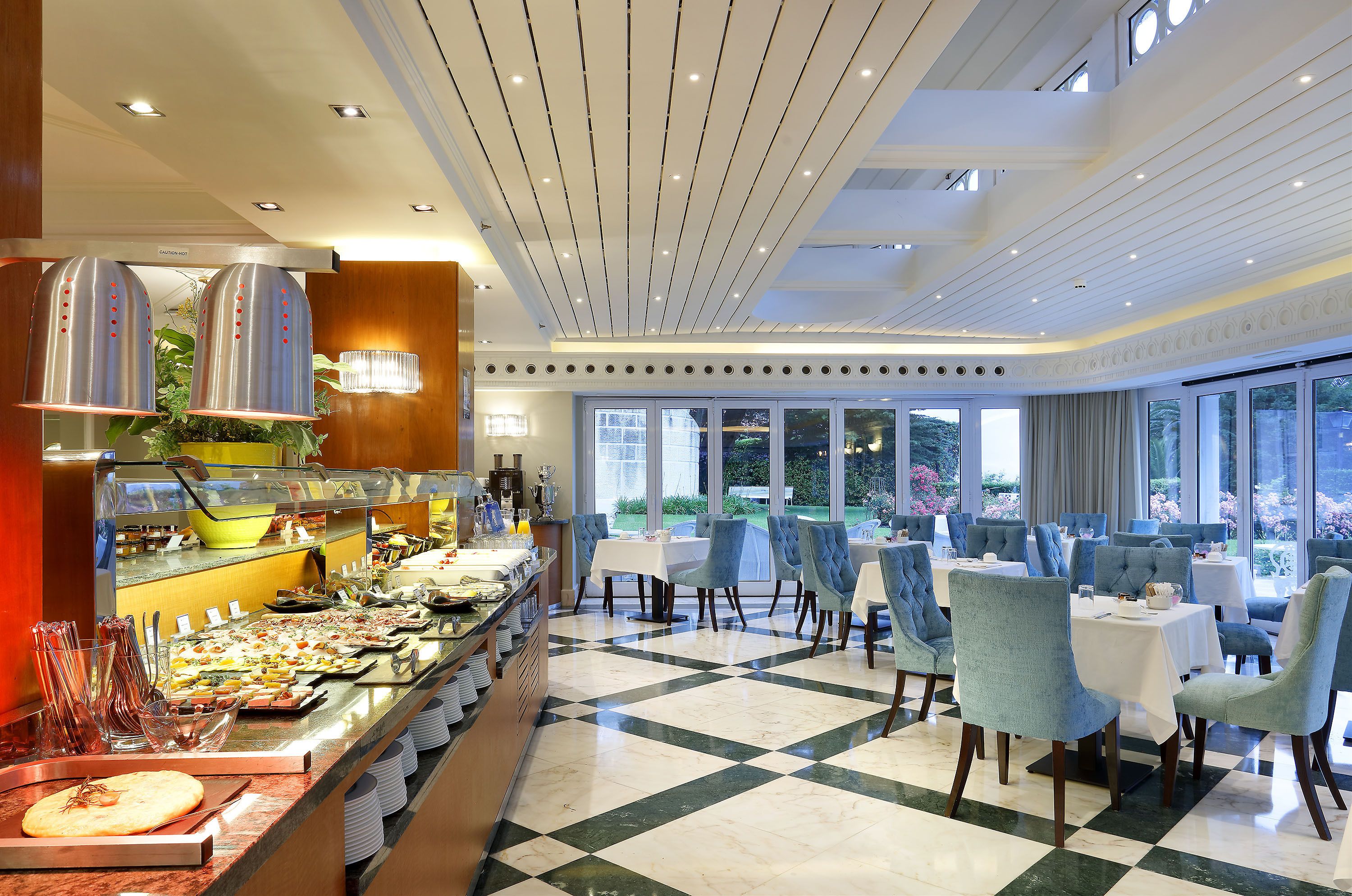 A buffet area with a variety of food items, a seating area with tables and chairs, and large windows providing a view of the outdoors.