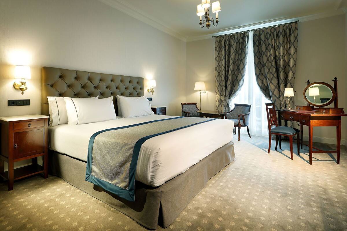 A hotel room with a large bed, bedside lamps, a desk with a mirror, and a chair.