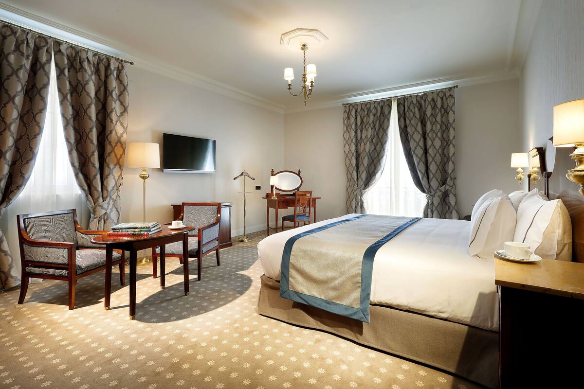 A hotel room with a bed, a desk, a chair, a television, and a lamp.