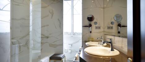 A modern bathroom with marble walls, a glass-enclosed shower, dual sinks, and a vanity with a mirror.