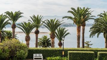 Jardín ajardinado con palmeras, un banco y vistas a un cuerpo de agua y montañas distantes.
