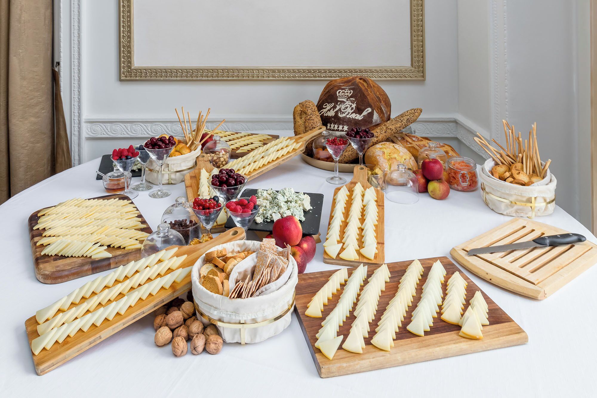 Una mesa con varios quesos, frutas y pan, dispuesta para un bufé.