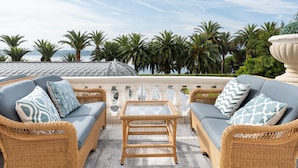 Un conjunto de sofá de mimbre con cojines estampados, una mesa de centro de vidrio y una vista de palmeras y una estructura en forma de cúpula al fondo.