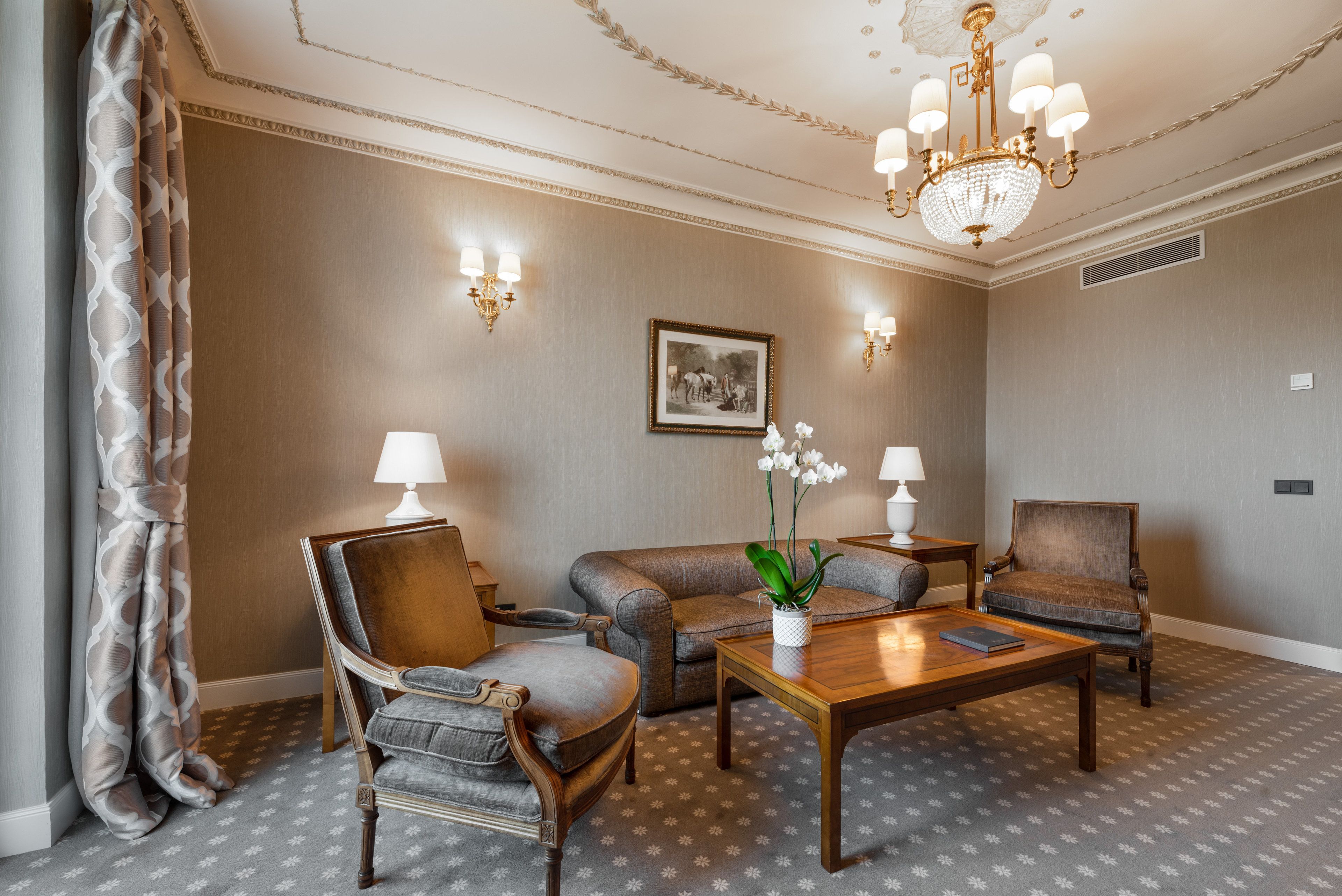 A room with a wooden coffee table, two armchairs, a sofa, and a chandelier.
