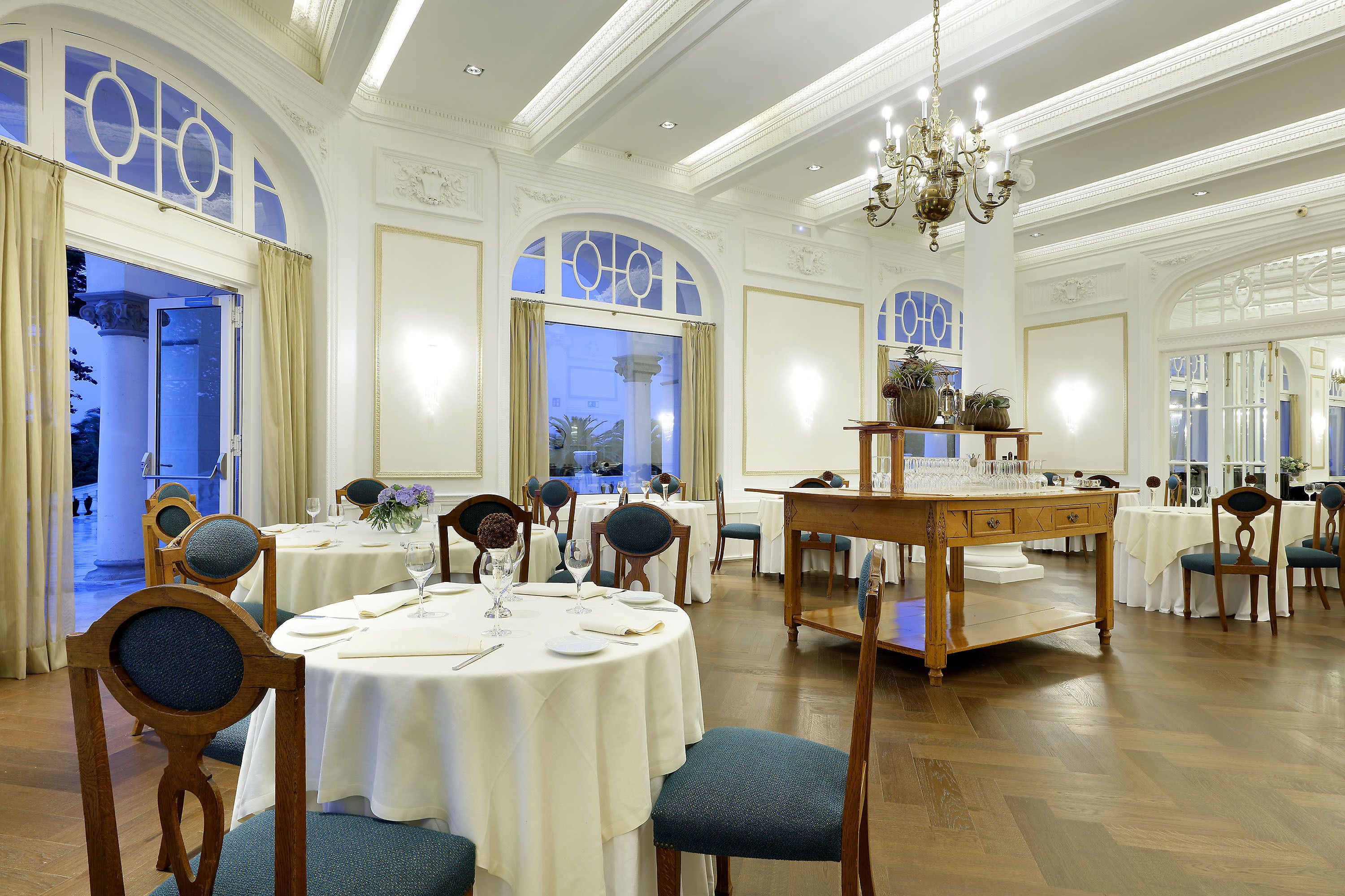 A formal dining room with round tables, chairs, and a central serving table.