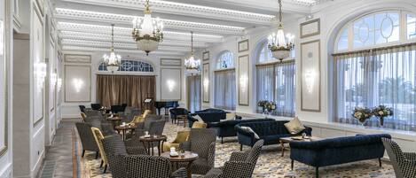 A spacious lobby with high ceilings, chandeliers, and a large seating area with sofas and armchairs.