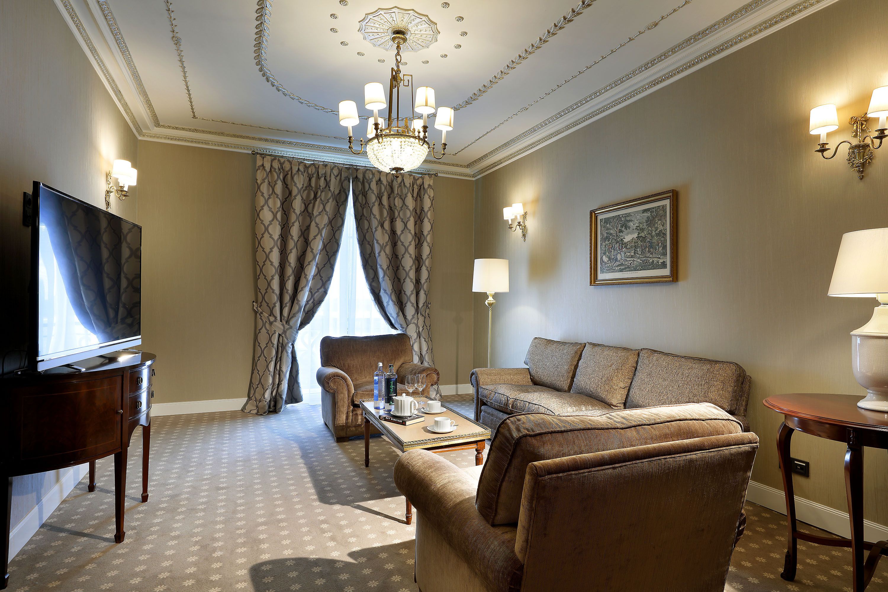 Una habitación de hotel con televisión, sofá, sillón, mesa de centro y candelabro.