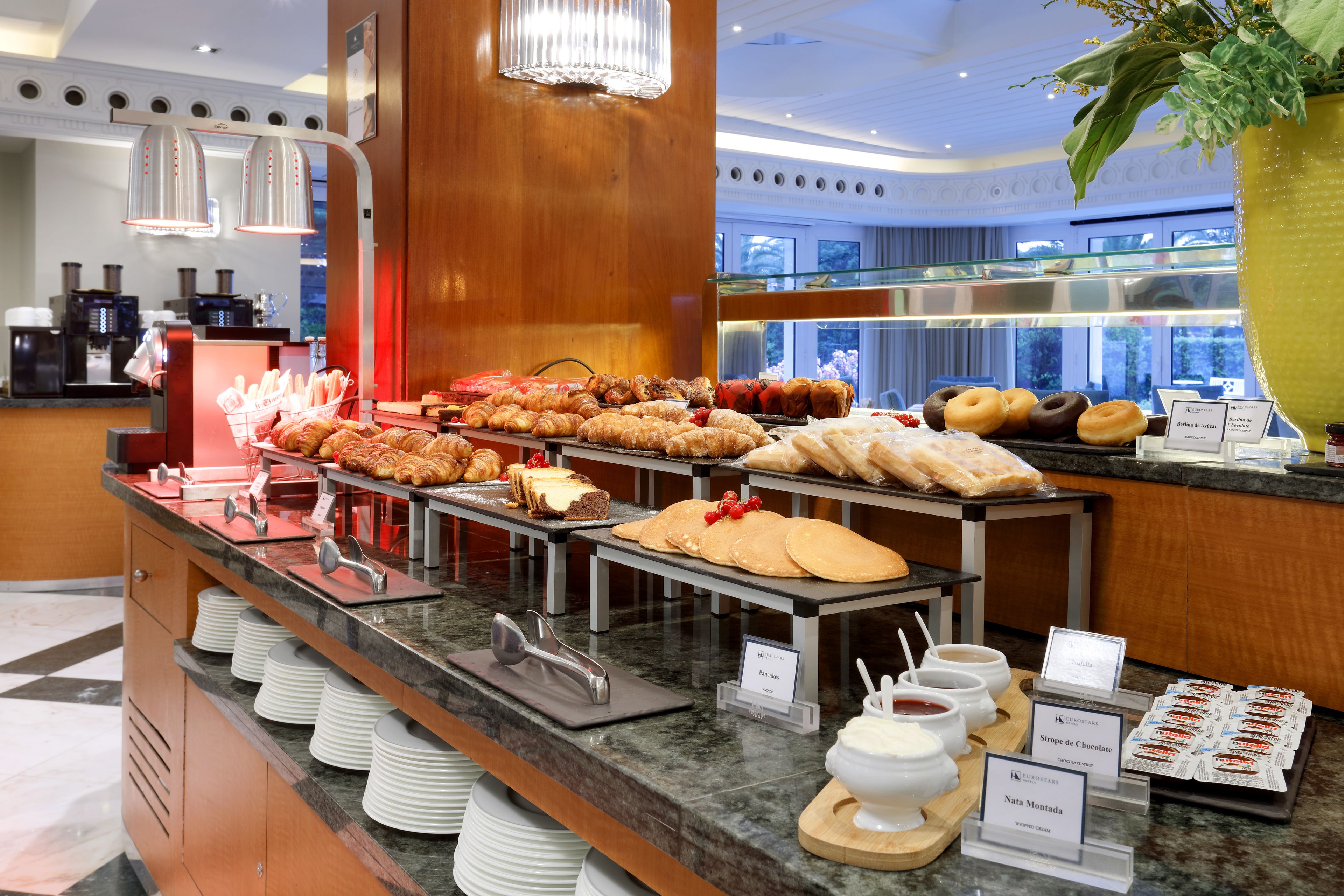 A buffet with various pastries and desserts, including croissants and cakes, with serving utensils and labels.
