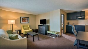 Ein Hotelzimmer mit Sofa, Sessel, Couchtisch, Fernseher, Küchenzeile und einem gerahmten Bild an der Wand.