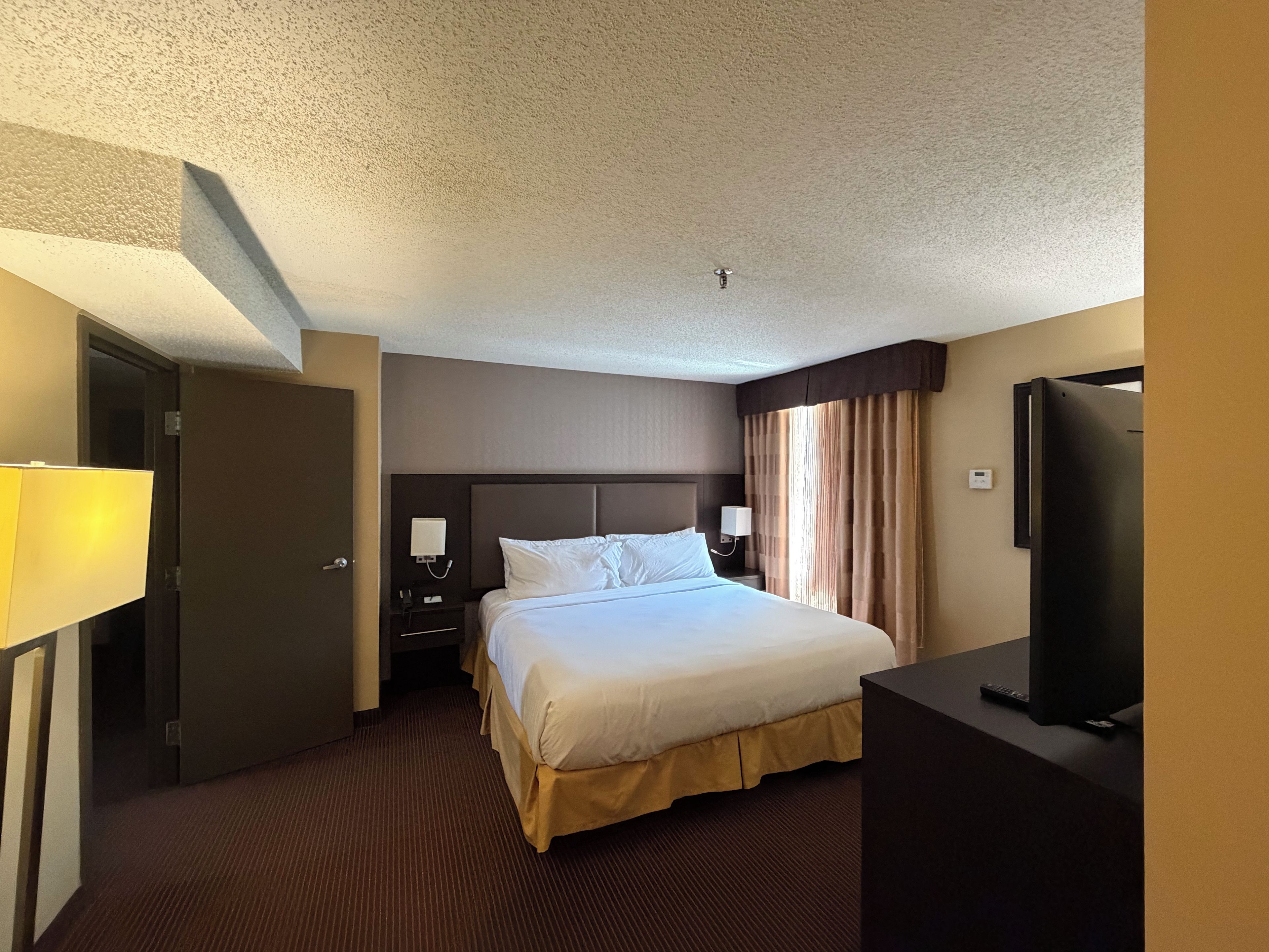Una habitación de hotel con una cama, un televisor, una mesita de noche y una puerta.
