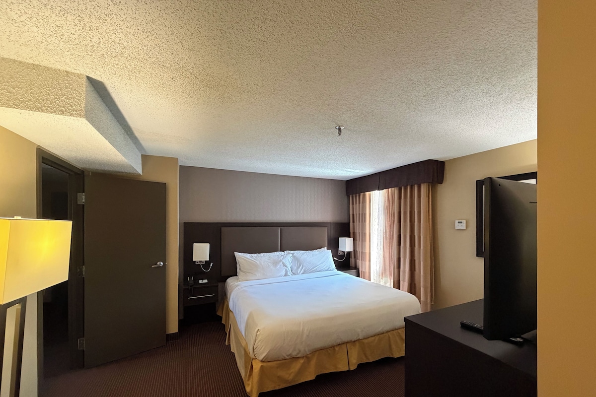 A hotel room with a bed, a television, a nightstand, and a door.